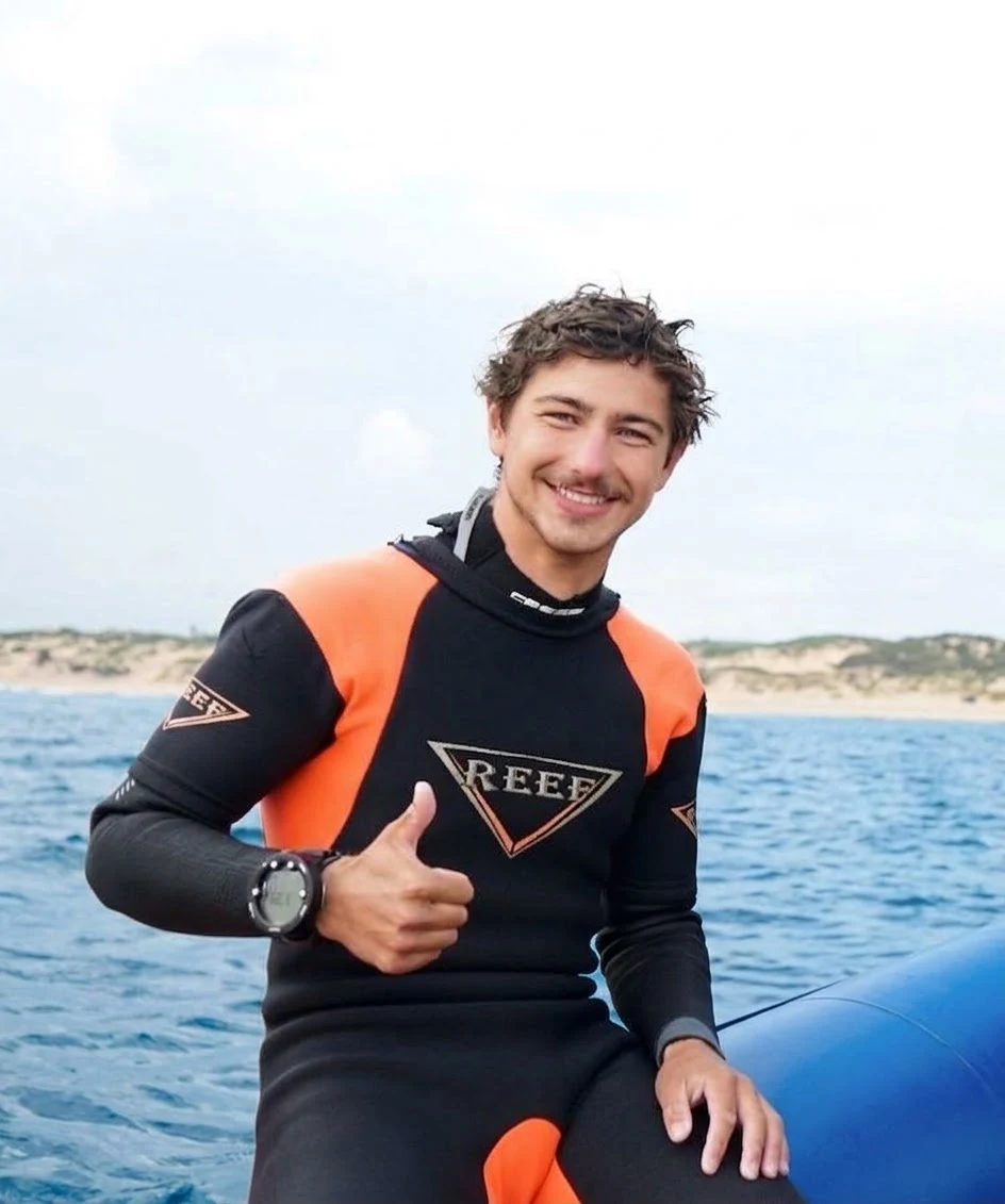 Miles Merhib smiling in a wetsuit and giving a thumbs-up aboard an inflatable boat