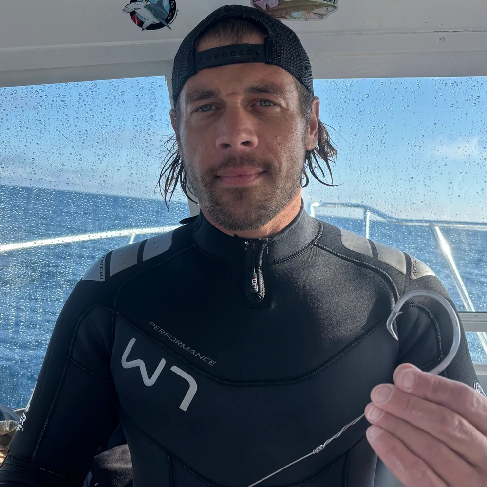 Nic Lombardo wearing a wetsuit and holding a hook aboard the boat